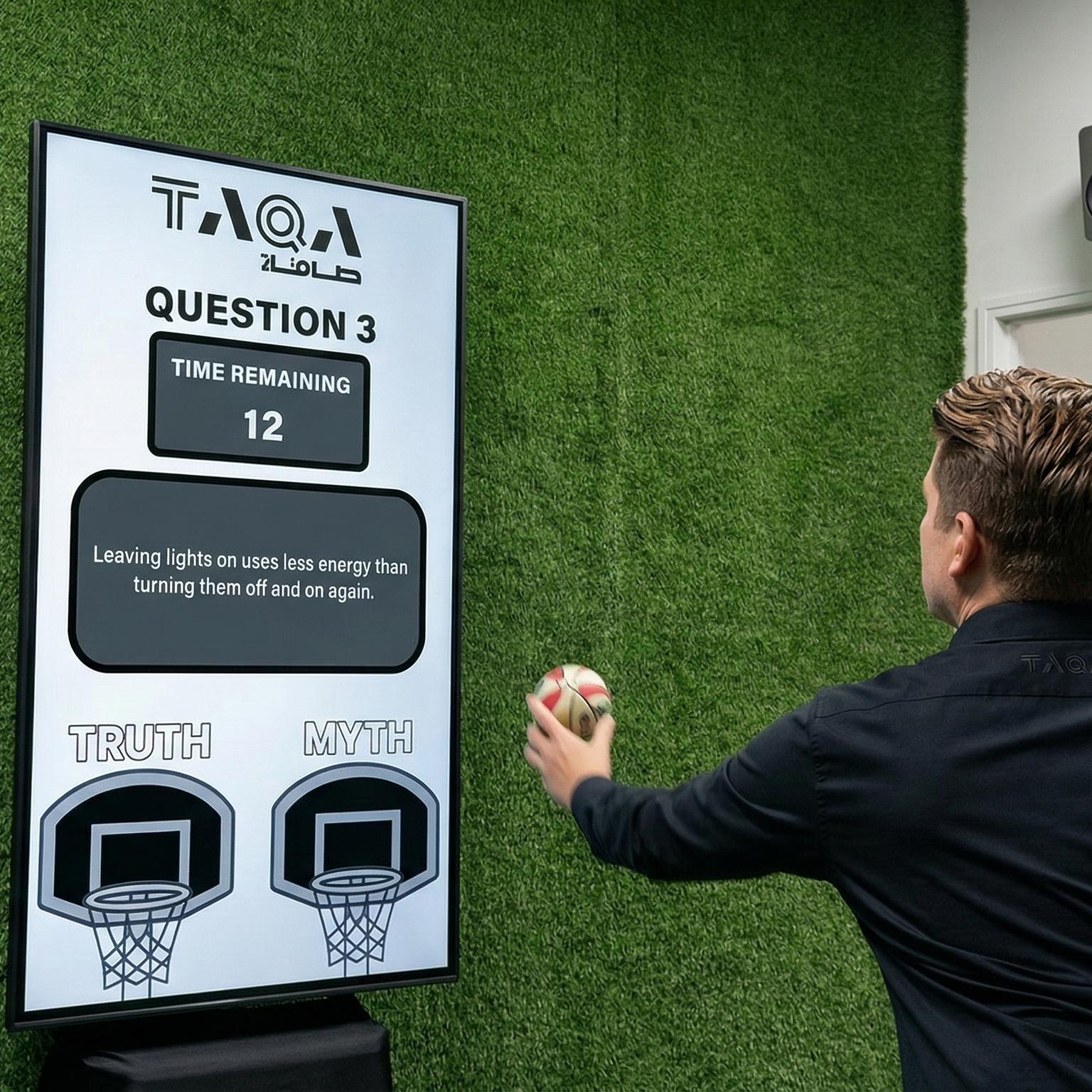 A guest throwing a softball at a large digital Truth or Myth display screen to lock in an answer at a high-energy corporate exhibition booth activation